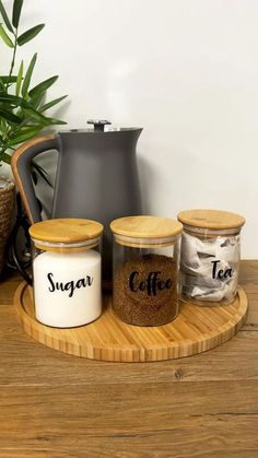 three jars with labels on them sitting on a wooden tray next to a potted plant