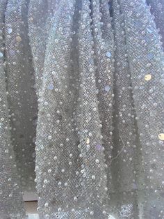 Beaded glitter net fabric for bridal gown. This is a beautiful rich fabric for wedding dress , wedding skirt. The color of the base is light grey or silver grey it has translucent glitters and subtle iridescent glitters. The base is net tulle covered with clear and iridescent glitter.  It is beaded on top with pearls beads and clear sequins. Embellished Tulle Fabric For Evening, Sparkling Tulle Sequin Fabric For Prom, Tulle Sequin Fabric For Prom, Elegant Sparkling Tulle Fabric For Evening, Sparkling Sequin Tulle Fabric For Evening, Embellished Sequin Tulle Fabric For Prom, Prom Glitter Tulle Fabric With Sequins, Glamorous Glitter Tulle Fabric For Evening, Glamorous Embellished Tulle Fabric For Party