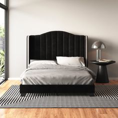 a bed with a black headboard sitting on top of a wooden floor next to a window