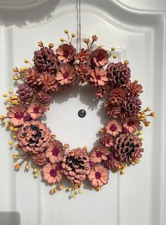 a wreath made out of pine cones hanging from a door handle on a white door