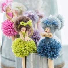 four little dolls sitting on top of a tin can filled with pom poms