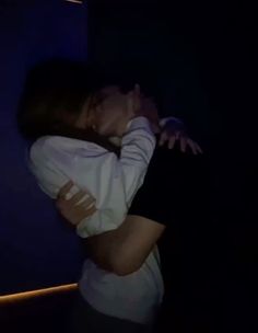 a man and woman kissing in the dark with their arms around each other's shoulders