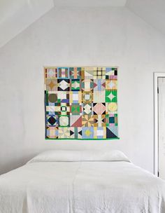 a bed with a quilt hanging on the wall above it in a room that has white walls