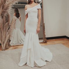 a woman standing in front of a mirror wearing a white dress with an off the shoulder neckline