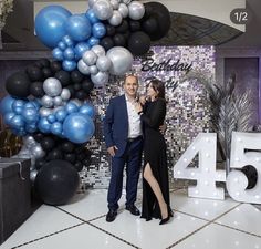 two people standing next to each other in front of balloons that spell the number forty five