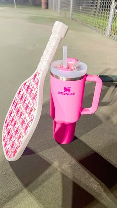 a pink cup with a toothbrush in it sitting on the ground next to a tennis court