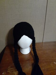 a white mannequin head wearing a black knitted hat on top of a wooden table