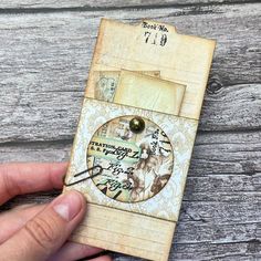 a hand holding an old fashioned clock on top of a piece of paper with writing