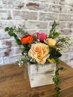 an arrangement of flowers in a wooden box on a table next to a brick wall