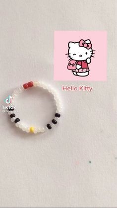 a hello kitty bracelet with black and white beads on it's side, sitting next to a pink background