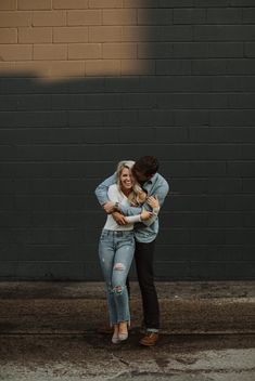 two people hugging each other in front of a brick wall