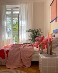 a bed with pink blankets and pillows in a bedroom next to a large painting on the wall