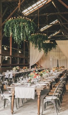 the tables are set up with white linens and greenery hanging from the ceiling