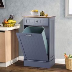 a gray trash can sitting on top of a wooden floor next to a table with fruit and vegetables