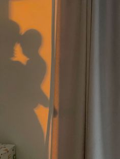 the shadow of a man and woman kissing in front of a window with yellow curtains