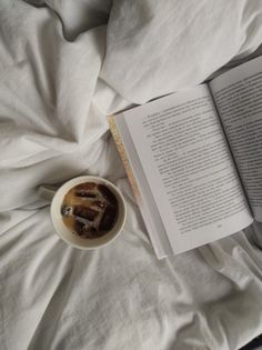 an open book sitting on top of a bed next to a cup of coffee