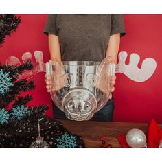 a person holding a clear glass in front of a christmas tree with decorations on it