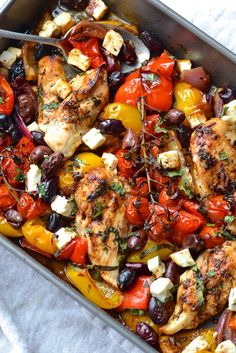 a pan filled with chicken and vegetables on top of a white table cloth next to a fork