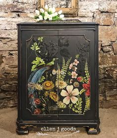 an ornate black cabinet with flowers painted on the front and sides, sitting in front of a stone wall