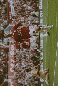 two soccer players in red and white uniforms standing on the field with their hands up