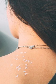 the back of a woman's neck with white birds on it and a chain around her neck