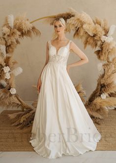 a woman in a wedding dress standing next to a wreath with feathers and flowers on it