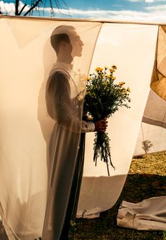 a man holding flowers standing next to a white sheet covered tent with the sun shining on him