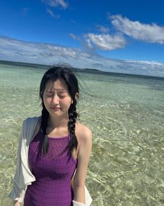 a woman standing in shallow water with her eyes closed and hands behind her back, looking at the camera