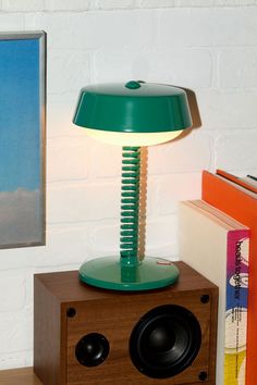 a green lamp sitting on top of a wooden table next to a bookshelf