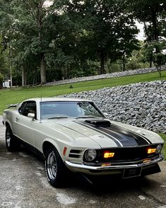 a white and black car parked in front of a stone wall with trees behind it