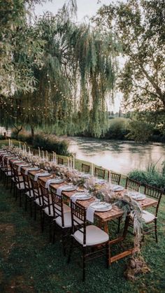 a long table set up for an outdoor dinner by the river