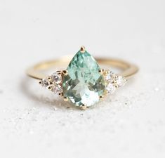 an aqua and white diamond ring with three diamonds around it on a white table top