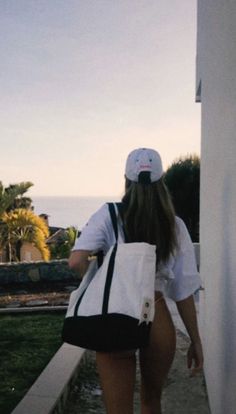 a woman walking down the sidewalk carrying a white tote bag on her back,