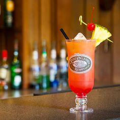 an orange drink with a cherry garnish on the rim sits on a bar