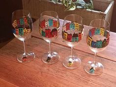 three wine glasses with different colored buildings on them sitting on a wooden table next to a potted plant