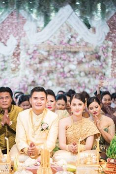 the bride and groom are sitting down for their wedding ceremony in thailand, where there is an abundance of flowers on the wall behind them