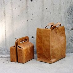 two brown leather bags sitting next to each other on the ground near a concrete wall