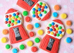 three decorated cookies with gummy bears and candy machines on a pink tablecloth background