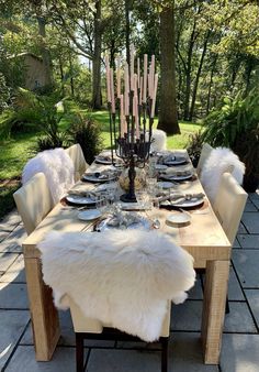 a dining table set with white chairs and place settings in the middle of a park