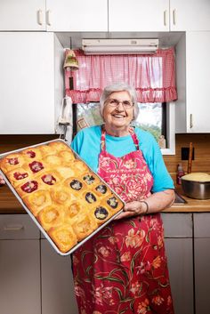 an older woman holding a pan full of pastries