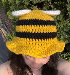 a woman wearing a yellow and black crocheted hat with horns on it's brim