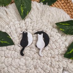 two small black and white cats laying on top of a blanket next to green leaves