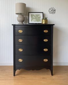 a black chest of drawers with gold handles and knobs on the bottom, next to a lamp