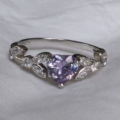 Brilliant sparkle with a captivating Lavender Cubic Zirconia heart shaped stone, this White Gold promise ring has a core of solid 925 Sterling Silver, making it hypoallergenic and built to last! The high-quality faceted lavender heart stone is 6mm (0.8 carat) and has a Mohs hardness of 8-1/2. Sprinkled generously with cubic zirconia rhinestones, this enchanting ring is accented by a nature-inspired tree branch and leaf design. It would make a great promise ring or engagement ring, as well as an Promise Ring Aesthetic, Ring With Purple Stone, Purple Engagement Rings, Lavender Jewelry, Lavender Jewellery, Gift Pictures, Heart Shaped Engagement Rings, White Gold Promise Ring, Heart Shaped Ring