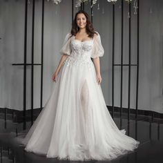 a woman in a white wedding dress standing on a black floor with flowers hanging from the ceiling