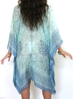 Our "Mid Length V-Neck Kaftan" in our beautiful Silk Tabi quality is an easy but elegant kaftan to throw on and go. This AQUA has an extremely airy feel & the Aqua color is truly stunning. The tunic has a Simple V neck front and back neckline. Great over swimwear or worn over a slip dress. The kaftan is a One Size fits all and can accommodate XS-2XL. Fabrication Content: 100% Tabi Silk Print Process: 100% hand made batik print, and every item is made by hand and a one of a kind item & limited items will be made in this style, Soft pink base with soft plum print. Size run: One Size Made in: Garment is custom made in LA - allow for 3 days in making plus transit time Care: Dry Clean Or rinse by hand in Luke warm water with small amount of detergent in the sink. The fabric is delicate so rise Blue Flowy Cover-up With Kimono Sleeves, Flowy V-neck Kaftan For Beach Cover-up, Blue Bohemian One Size Kaftan, Blue Bohemian V-neck Kimono, Green Flowy V-neck Kimono, Flowy Kaftan With Kimono Sleeves For Festivals, Flowy Festival Kaftan With Kimono Sleeves, Blue One Size Kaftan For Beach, Festival Flowy Kaftan With Kimono Sleeves