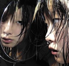 two women looking at their faces in the mirror with hair flowing over them and one woman's face partially obscured by her reflection