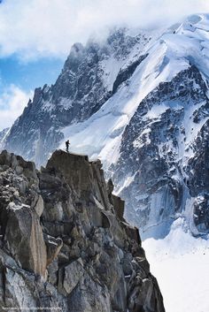 a man standing on top of a snow covered mountain next to a large rock formation