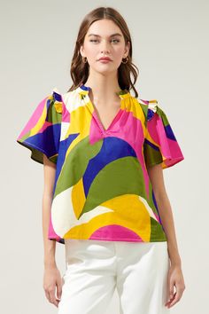 Introducing the whimsical wonder of the Rio Abstract Split Neck Poplin Top– where comfort meets color in a playful dance of poplin cotton perfection! Adorned with small ruffle ends on the shoulders and around the neckline plus a smooth outlined deep v-cut frame. So, go ahead, seize the day, and let your vibrant spirit shine through!- Ruffle detail- Split neckline- Short sleeves- Relaxed fit- Color: Khaki MultiSize + Fit - Model is 5'8" and wearing size XS- Measurements taken from size S - Chest: Printed Cotton Top With Flutter Sleeves, Colorful Cotton V-neck Tops, Multicolor Cotton Ruffle Sleeve Tops, Multicolor Cotton Top With Ruffle Sleeves, Multicolor Cotton Tops With Ruffle Sleeves, Printed Cotton Blouse With Ruffle Sleeves, Multicolor Cotton Blouse With Ruffle Sleeves, Playful Ruffle Flutter Sleeve Tops, Playful Tops With Ruffles And Flutter Sleeves