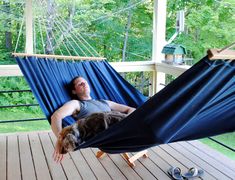 a man laying in a hammock on a deck with his dog, sleeping